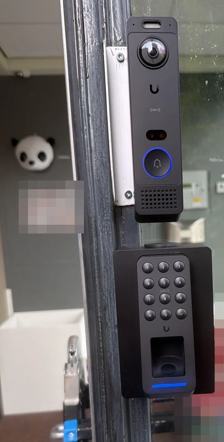 UniFi G6 Entry-deurbel met camera en daaronder een zwarte UniFi G3 Reader Fingerprint met cijfertoetsen en vingerafdruklezer, op een zwart opbouwkastje aan het kozijn van de voordeur van een kinderdagverblijf