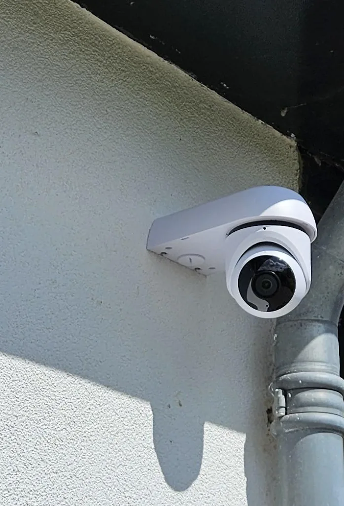 Witte UniFi G6 Turret-camera op een hoekbeugel onder de dakrand, vlak naast de regenpijp