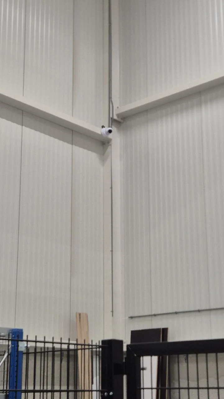 Witte UniFi G6 Turret-camera hoog in de hoek van een paneelwand