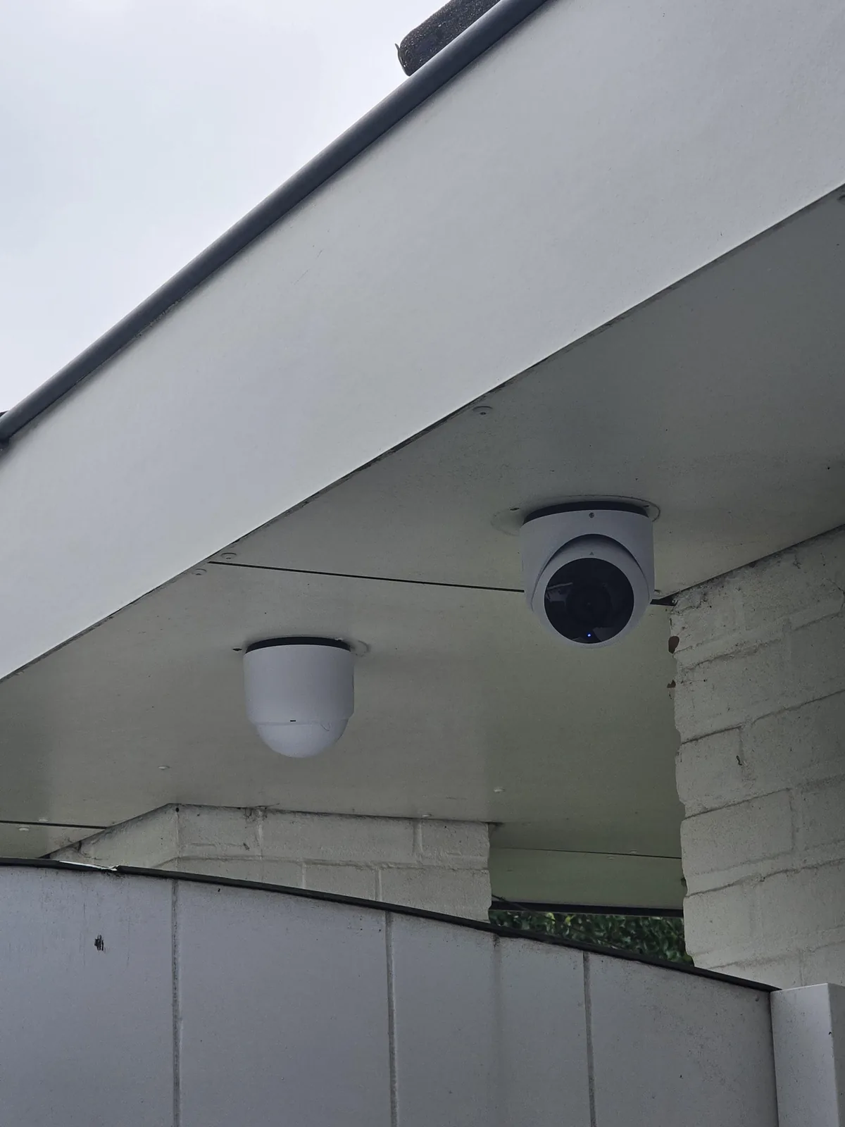 Witte UniFi G6 Turret onder een wit overstek, naast een witgeschilderde bakstenen gevel