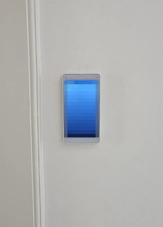 Wit UniFi Intercom Viewer-scherm aan de wand in de hal, naast een oude houten deurlijst; de schermtekst is onleesbaar gemaakt