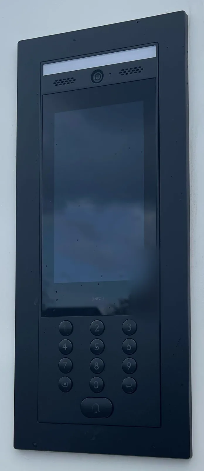 Zwarte UniFi-intercom met camera, scherm, NFC en codeklavier, ingebouwd in een witte hekpilaar