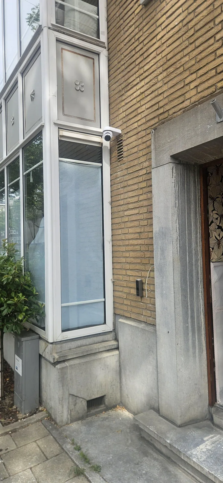 Zwarte UniFi-intercom naast de voordeur, met een camera hoog op de hoek van de gevel