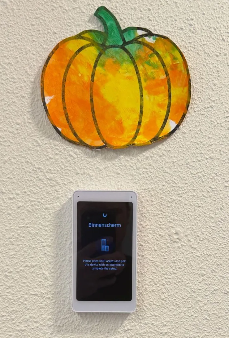 Net opgehangen UniFi Intercom Viewer op een witte wand onder een geschilderde pompoen, met op het scherm de koppelstap in UniFi Access