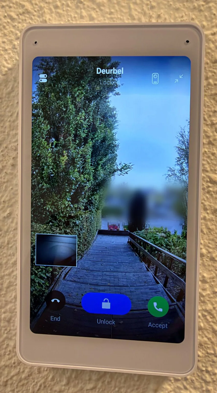 Witte UniFi Intercom Viewer aan de wand tijdens een oproep van de deurbel: live beeld van het pad naar de voordeur met de knoppen End, Unlock en Accept