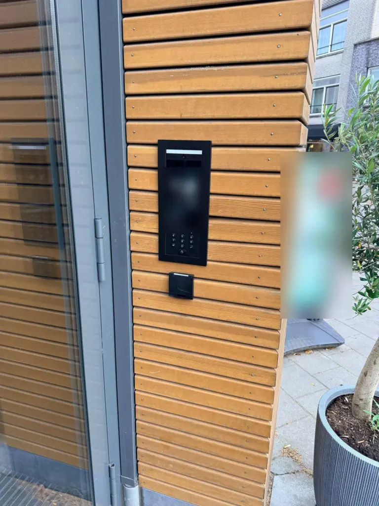Zwarte UniFi G3-intercom ingebouwd in een gevel van houten latten naast de glazen voordeur, met een paslezer eronder