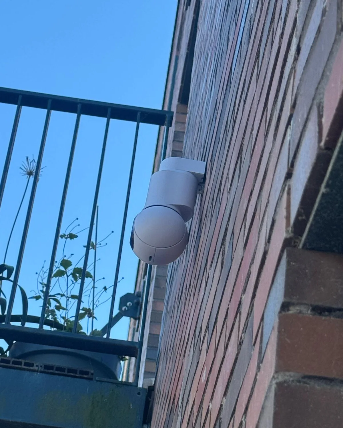 Witte PTZ-camera aan een bakstenen gevel, naast een balkon met een zwart hekwerk