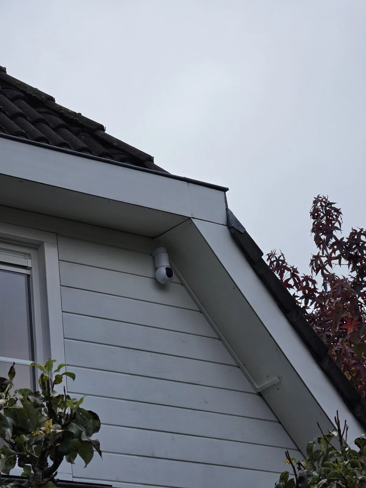 Witte UniFi PTZ-camera hoog op een lichte topgevel, met een klein wit kabelgootje onder de boeiboord