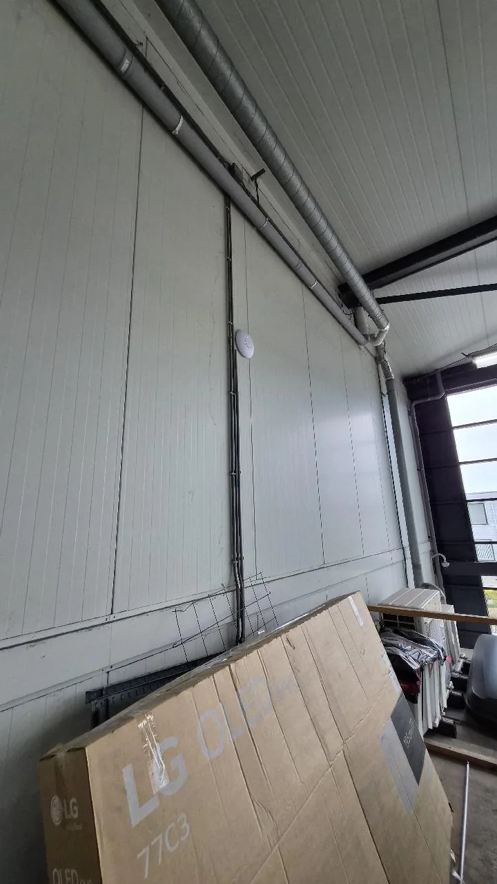 UniFi U7 Pro hoog op de wand van de werkplaats van een autoverhuurbedrijf in Utrecht, de kabel in een strakke goot naar beneden