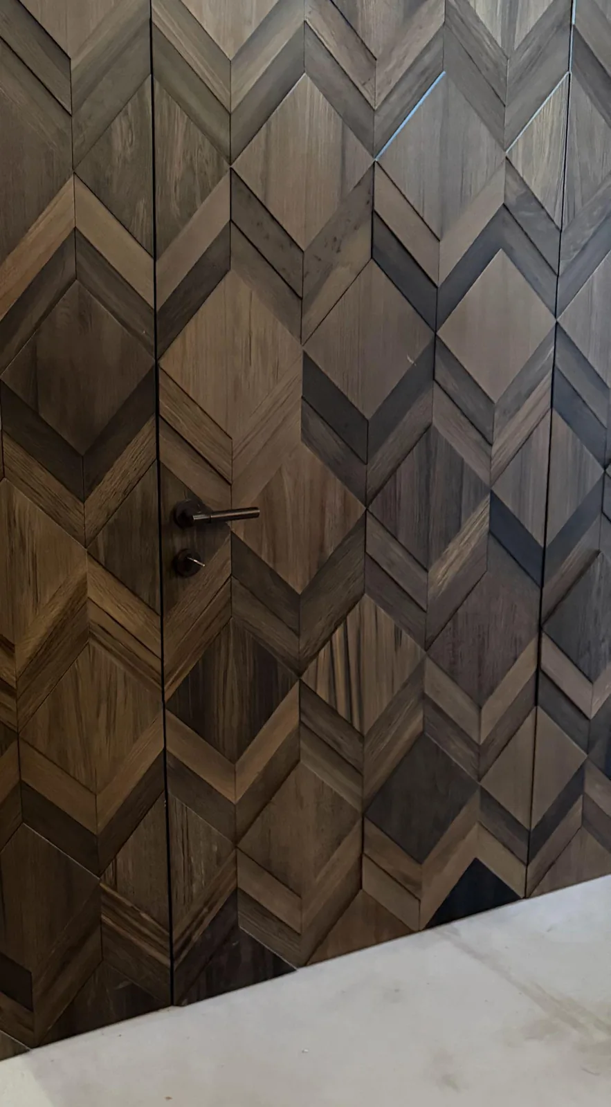 Deur zonder zichtbaar kozijn in een wand van houten ruitpanelen, alleen de deurkruk verraadt hem