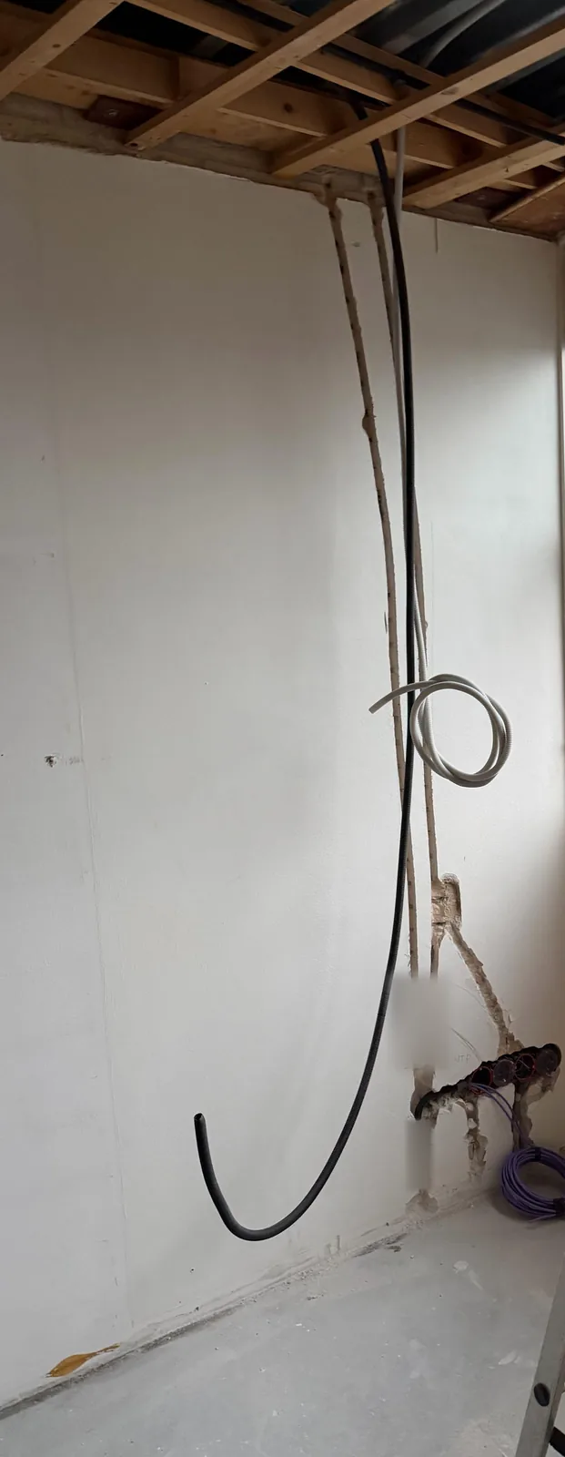 Flexbuizen lopen vanaf het plafond in sleuven omlaag naar een rij inbouwdozen, met een rol paarse Cat6 op de vloer