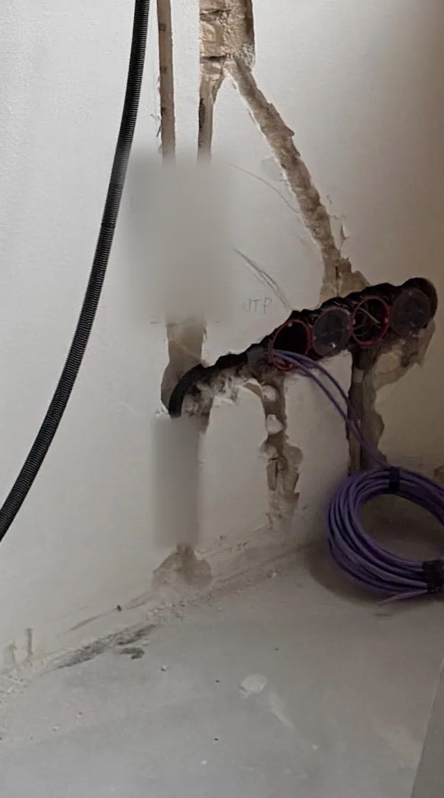 Rij inbouwdozen onderaan de muur met paarse Cat6-kabels en een opgerolde rol netwerkkabel ernaast