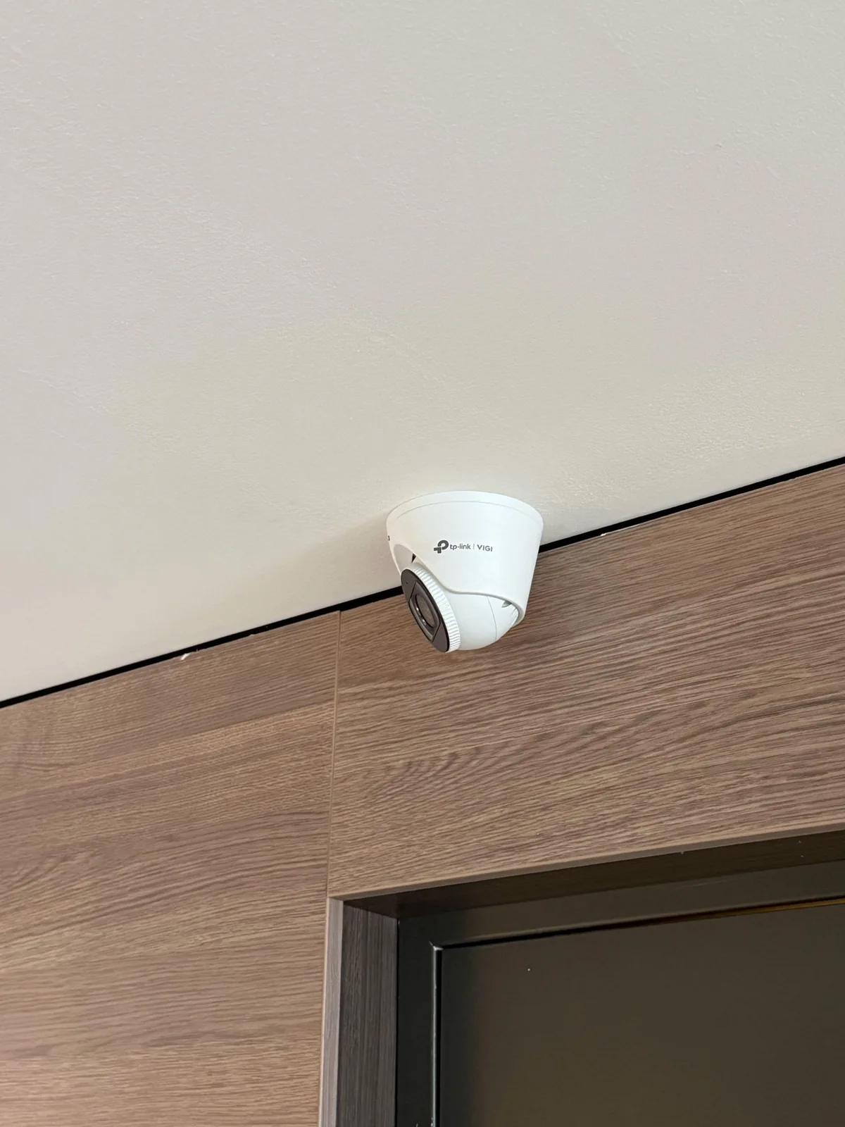 Witte VIGI-turretcamera aan het plafond boven een houten wand en een deur