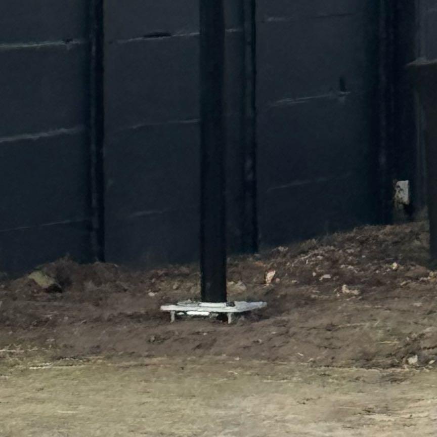 Onderkant van de zwarte mast op een voetplaat in de grond naast de stal