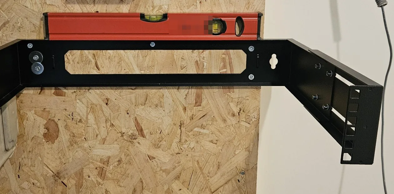 Zwarte wandbeugel voor het patchrek op een wand van OSB, met een rode waterpas erop