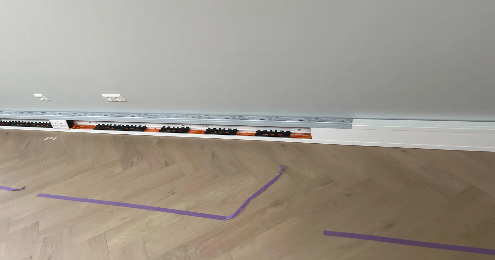 Wandgoot langs een lange lichte wand in een kantoor in Utrecht, het rechterdeel al dicht, links nog open met de kabels zichtbaar