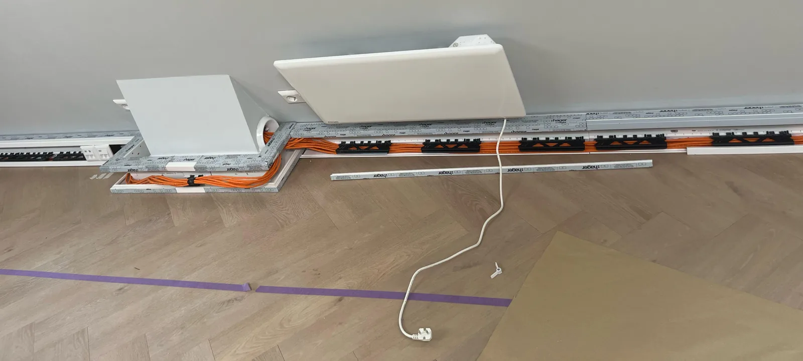 Wandgoot met oranje netwerkkabels die om een uitsparing in de wand heen loopt, de deksels liggen er nog naast