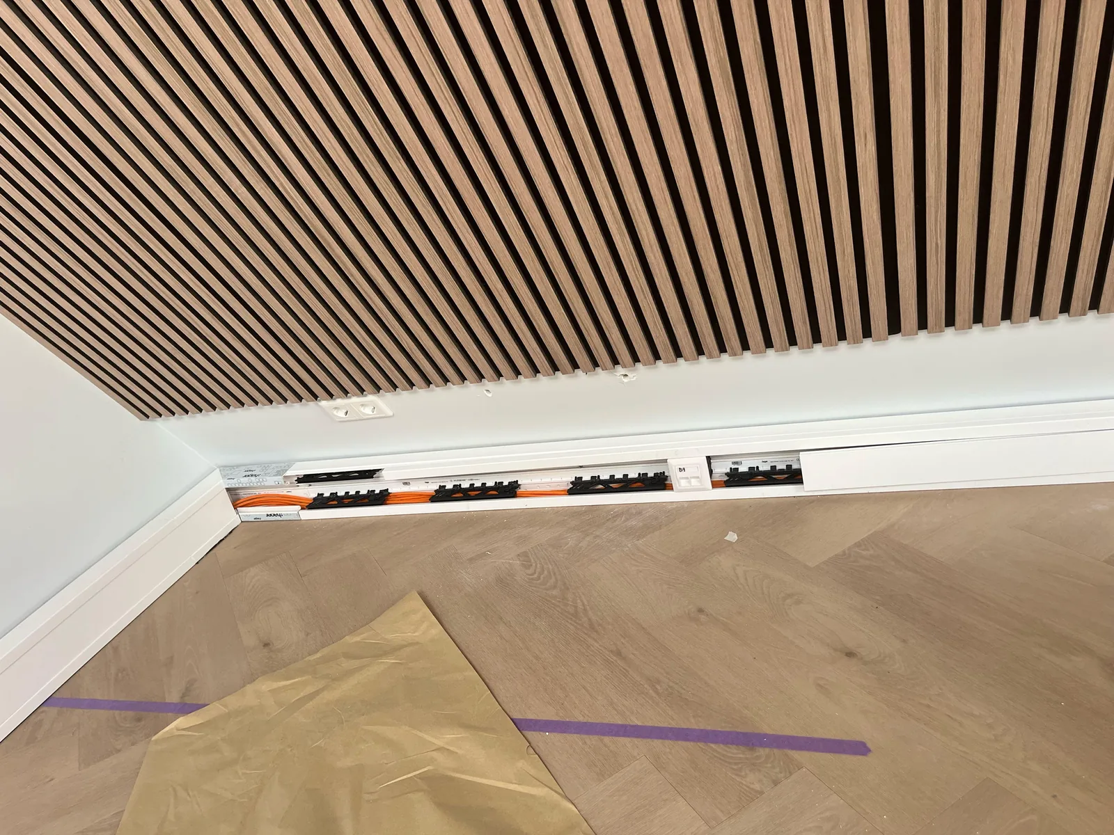 Lange wandgoot langs de vloer van een kantoorruimte met een houten lamellenplafond, deels al met de witte deksel erop