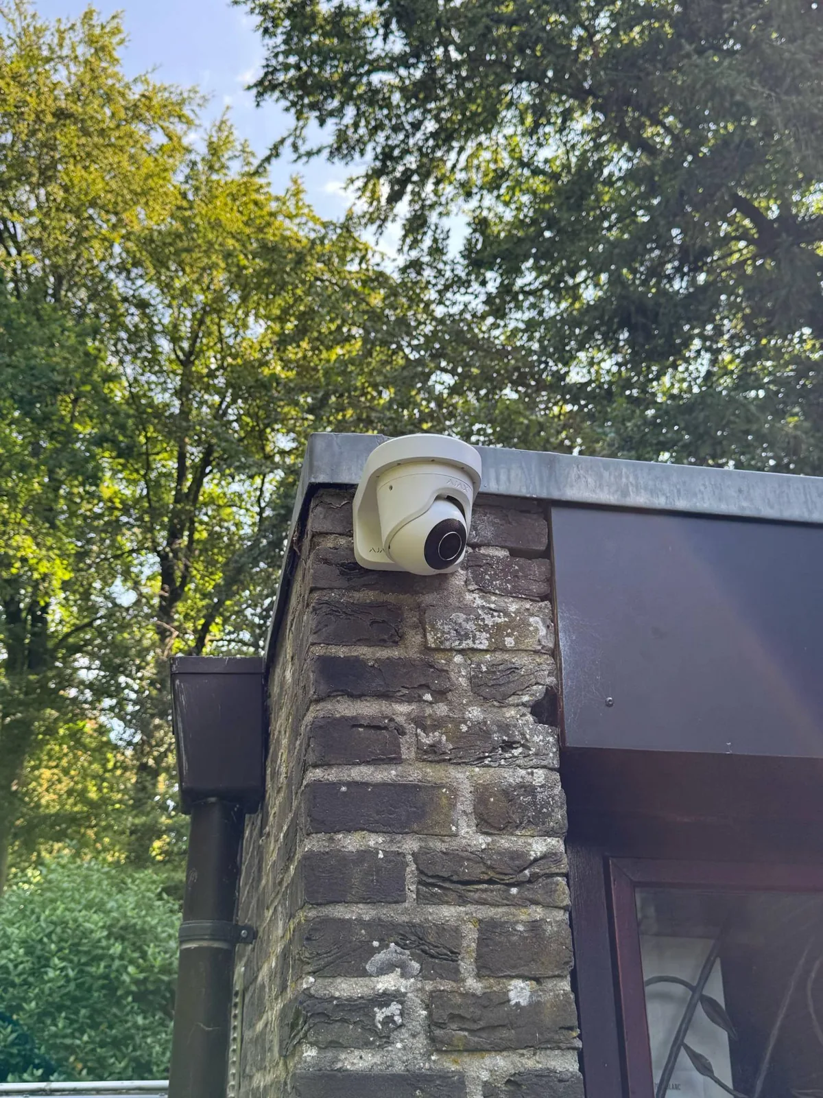 Witte Ajax-camera op de hoek van een bakstenen bijgebouw, net onder de daktrim, bij een woning in Maarn