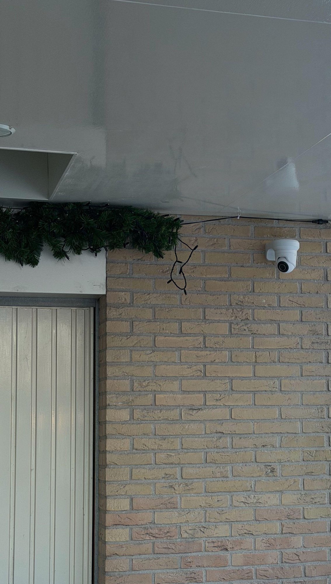 Witte camera op de bakstenen muur onder de overkapping, naast de garagedeur, in de sneeuw