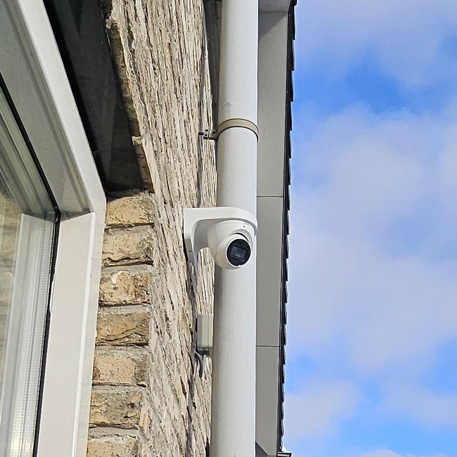 Witte camera op een witte beugel tegen de bakstenen gevel, direct naast de regenpijp