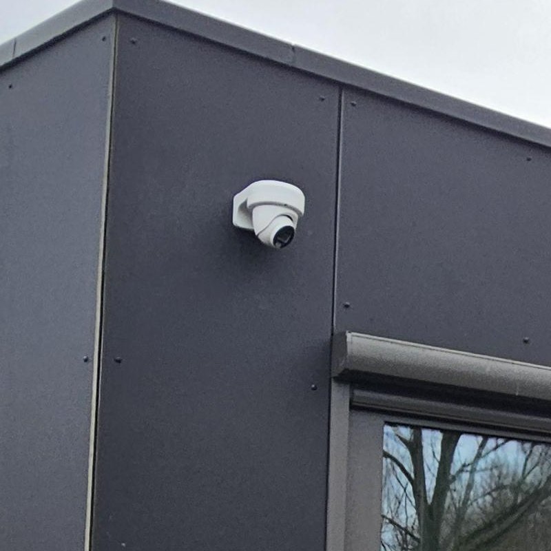Witte camera hoog op een donkere gevel, net onder de dakrand boven het raam