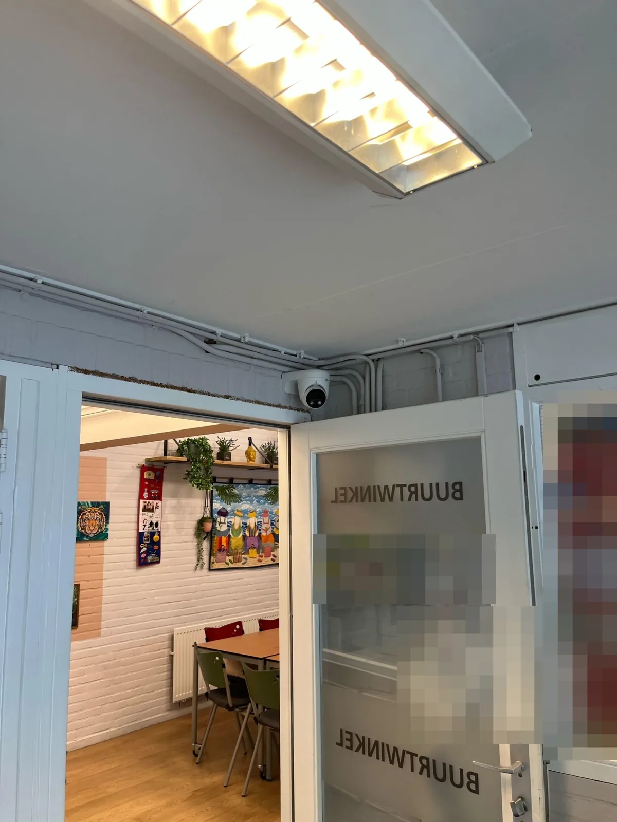 Witte Dahua TiOC-camera in de hal van een buurtpand in Haarlem, boven de deur naar de buurtwinkel