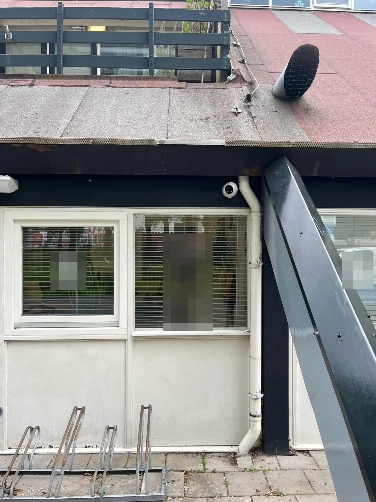 Witte Dahua TiOC-turretcamera onder de zwarte dakrand, naast de witte regenpijp, boven de ramen van een nis