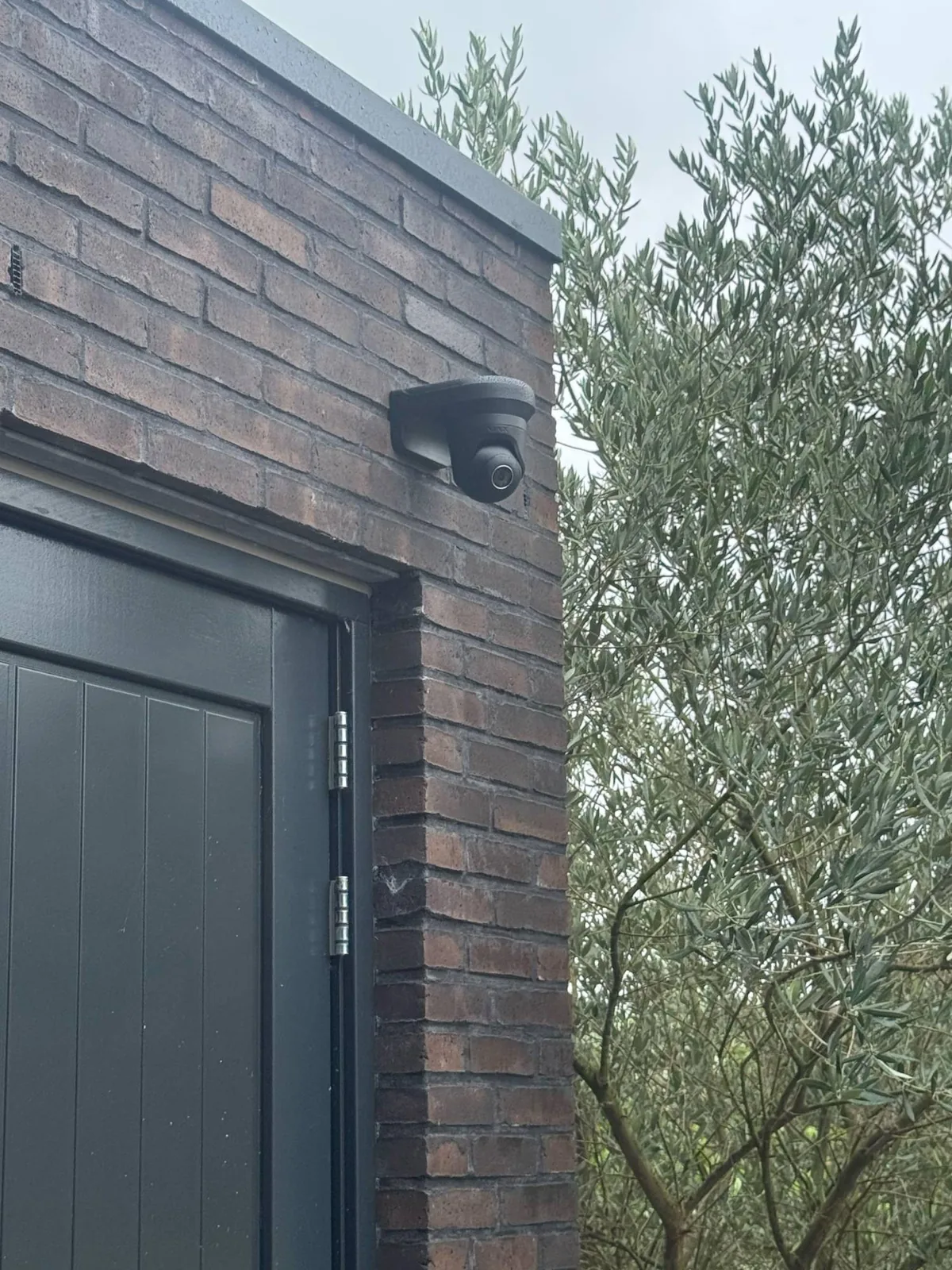 Zwarte Ajax-camera boven een deur op donkere baksteen, bij een woning met Ajax-alarm in Blaricum