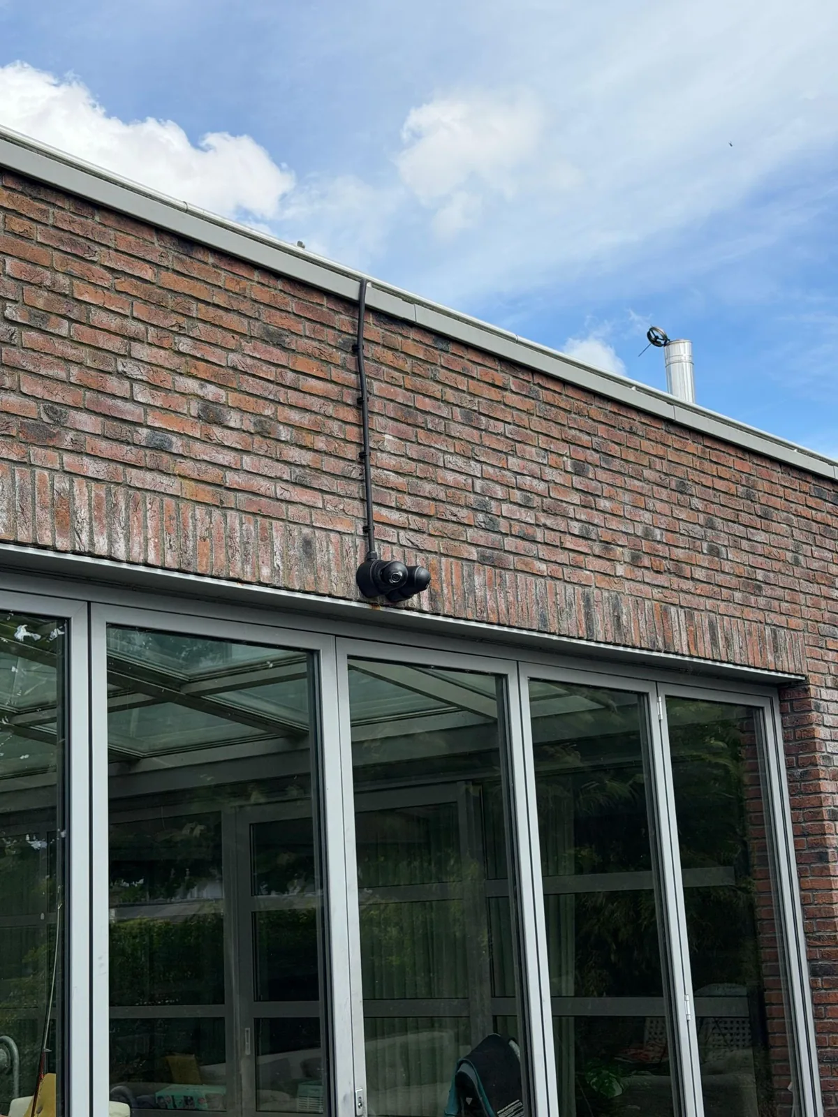 Twee zwarte Ajax-camera&rsquo;s rug aan rug boven een vouwpui, met de kabel in zwarte buis, bij een woning in Kropswolde