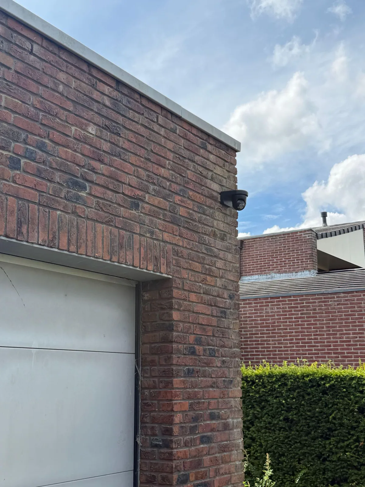 Zwarte Ajax-camera op de hoek van een bakstenen gevel boven een garagedeur, bij een woning in Kropswolde