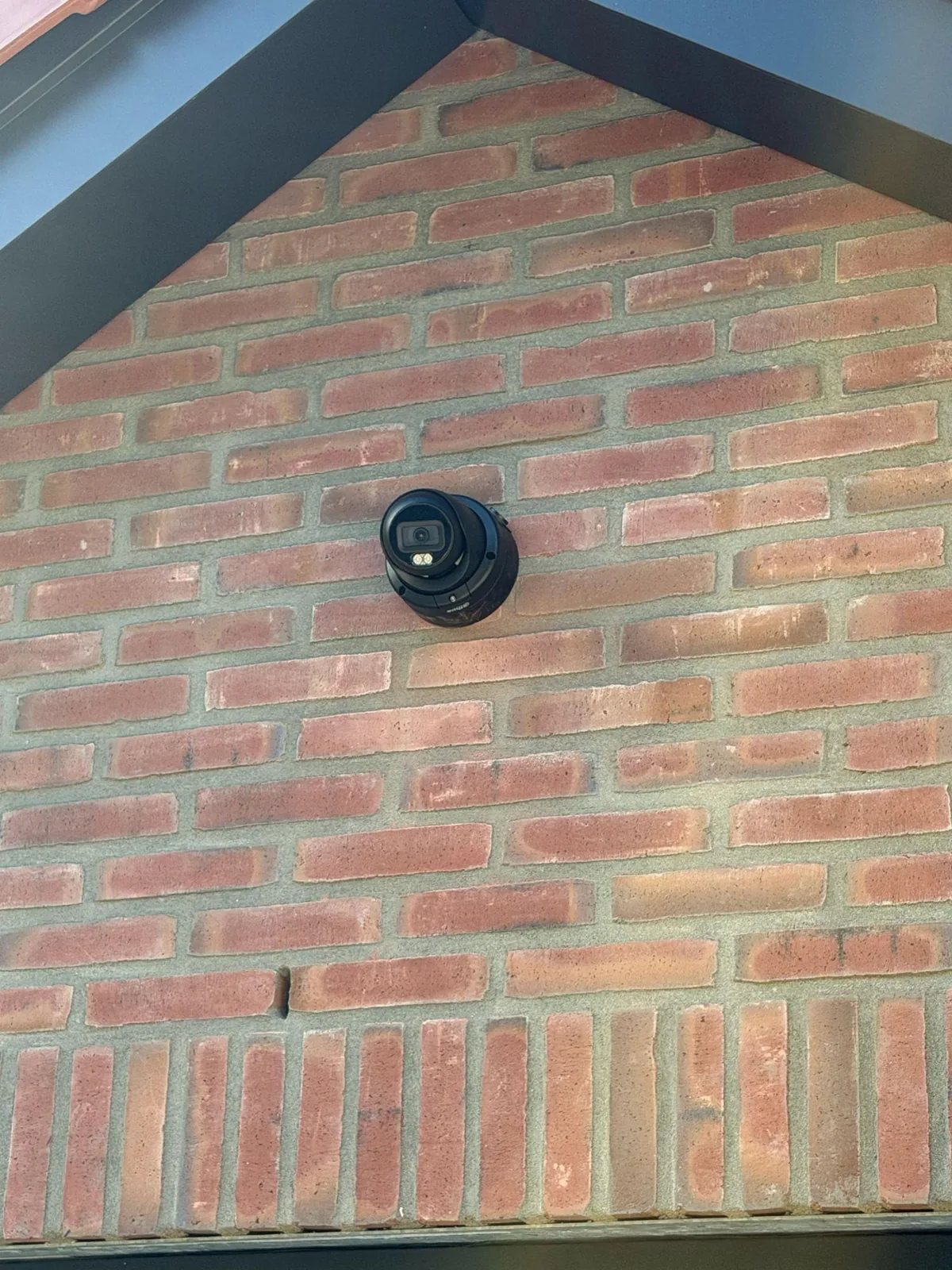 Zwarte Dahua-turretcamera van 8 MP in de punt van een bakstenen topgevel, onder zwarte boeiboorden