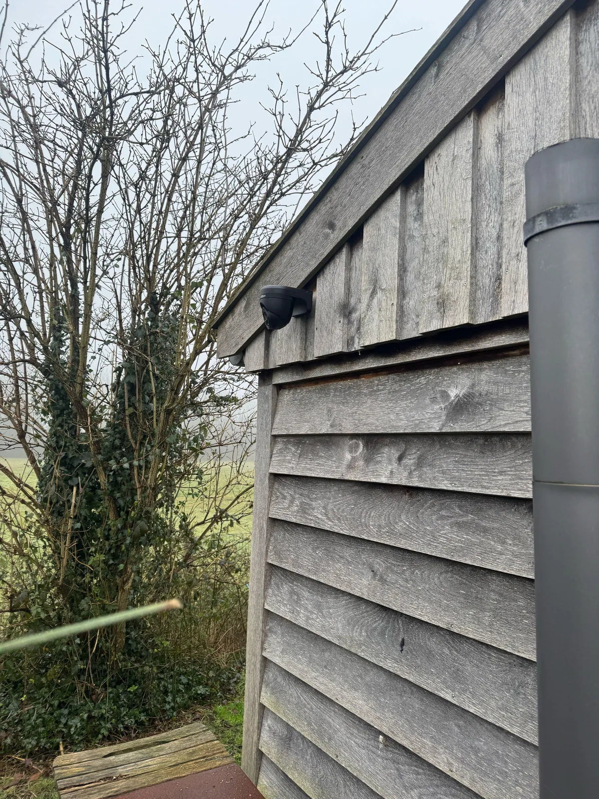 Zwarte Dahua-turret onder de dakrand van een houten stal, met het weiland erachter