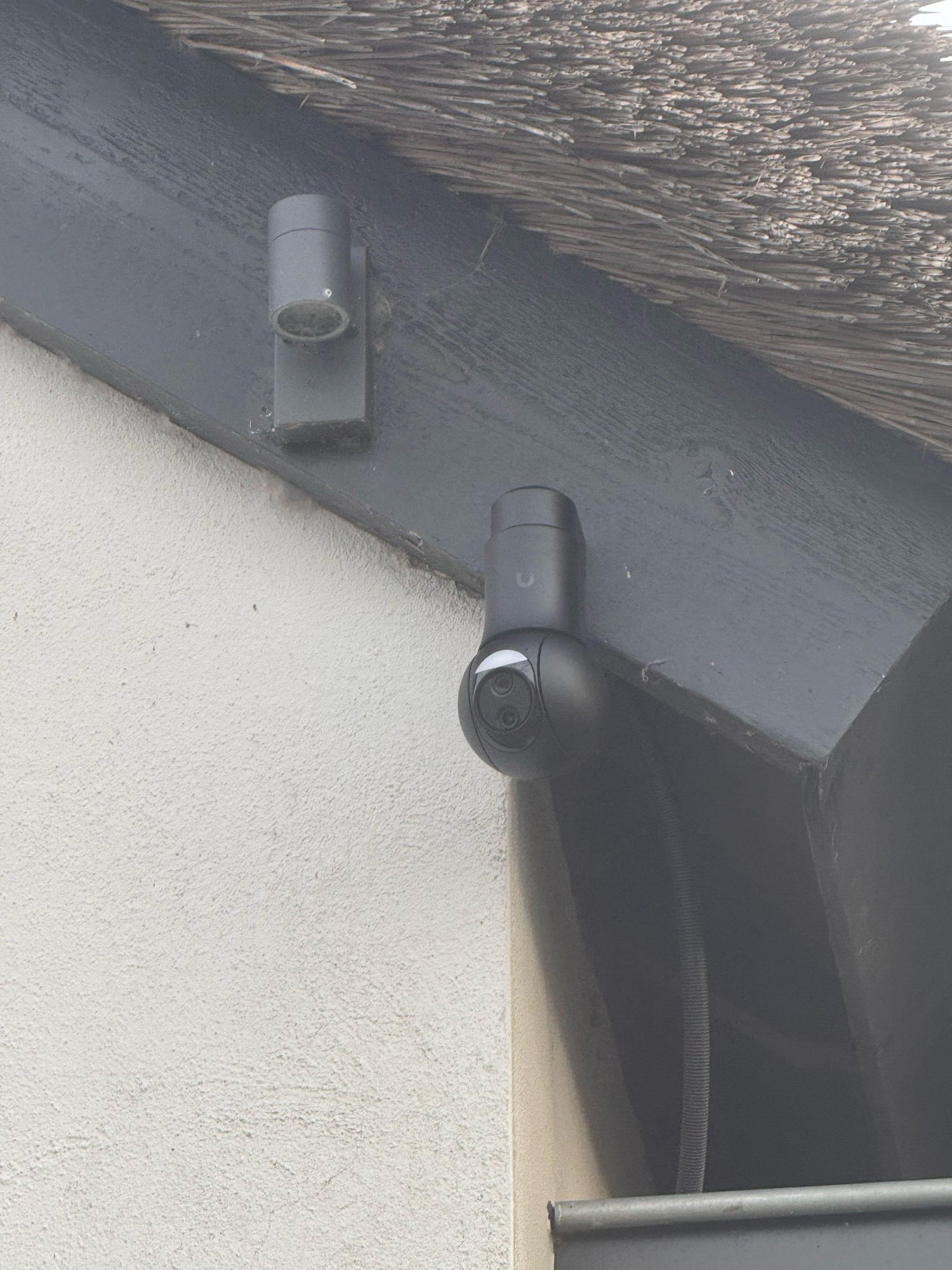 Zwarte turretcamera op een donkere dakrand onder het riet, met de kabel weggewerkt